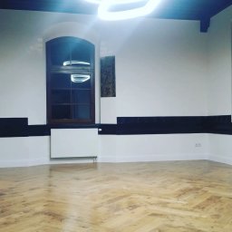 ELISA BAU SPÓŁKA Z OGRANICZONĄ ODPOWIEDZIALNOŚCIĄ - Jasny parkiet w jodełkę, białe ściany z ciemnym pasem, okno z łukiem i grzejnik. Nowoczesne oświetlenie sufitowe. Puste, odnowione wnętrze z charakterem.