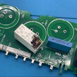 B&G Electronics - Uszkodzony przekaźnik na zielonej płycie falownika z elementami elektronicznymi. Widoczne kondensatory, rezystory i oznaczenia. Detal naprawy elektroniki.