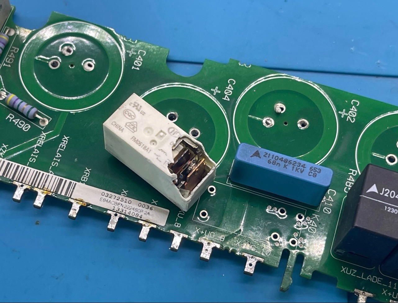 Uszkodzony przekaźnik na zielonej płycie falownika z elementami elektronicznymi. Widoczne kondensatory, rezystory i oznaczenia. Detal naprawy elektroniki.