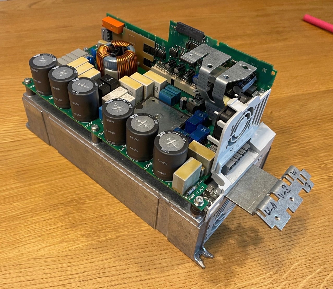 Otwarty falownik na drewnianym stole. Widoczne kondensatory, radiator, wentylator i płytka drukowana. Elementy elektroniczne w zbliżeniu, ukazujące skomplikowaną budowę.