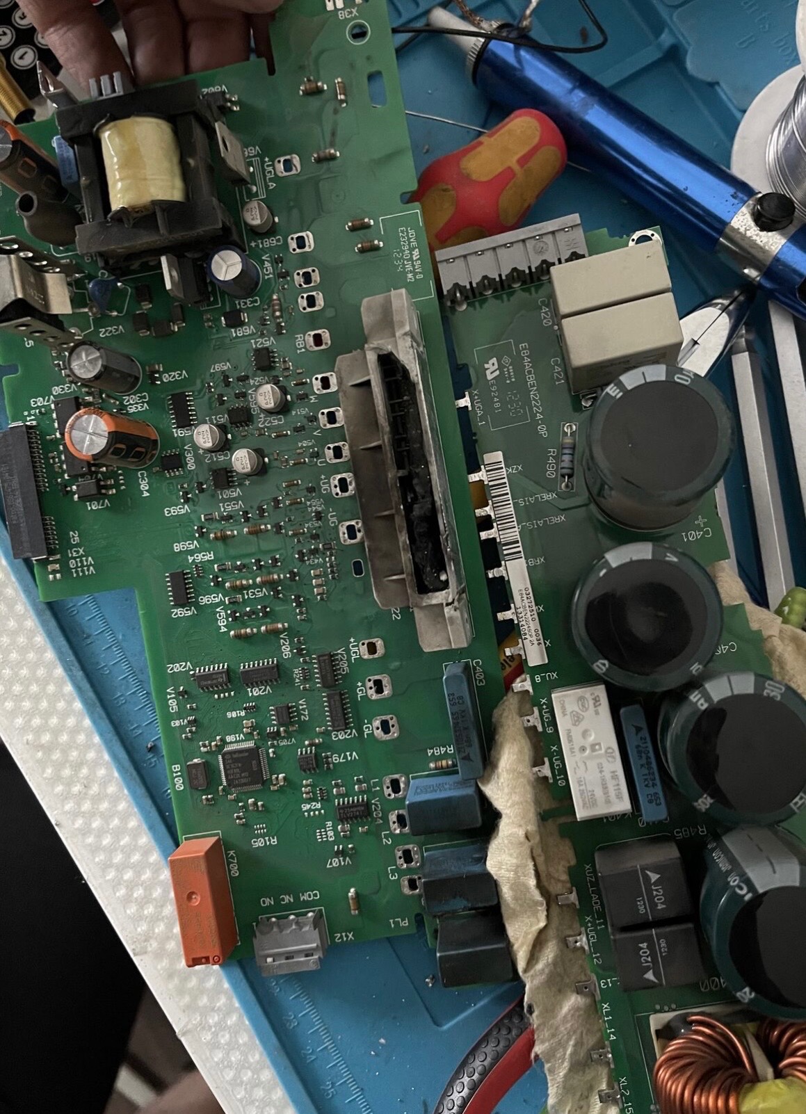 Uszkodzona płyta falownika z widocznymi elementami elektronicznymi, narzędzia obok. Detaliczne ujęcie podkreśla złożoność naprawy elektroniki przemysłowej.