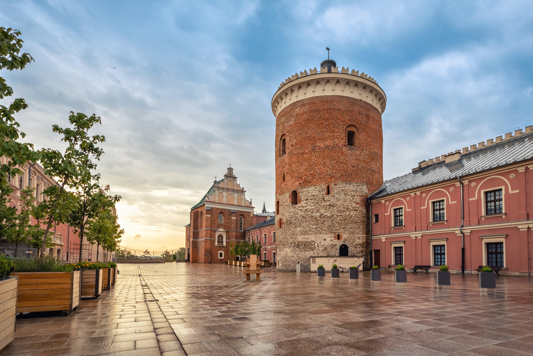 Zamek w Lublinie w porannym świetle. Ceglana wieża, renesansowa architektura, mokry bruk placu. Widok na zabytek z perspektywy pieszego, po deszczu.