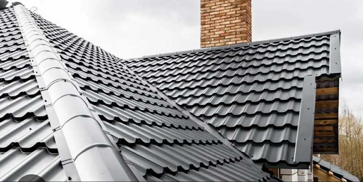 Grafitowy dach z blachodachówki modułowej, z widocznym kominem z cegły i orynnowaniem. Ujęcie z dołu, podkreślające regularność wzoru i precyzję wykonania.