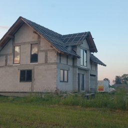 USŁUGI OGÓLNOBUDOWLANE MATEUSZ ZAKRZEWSKI - Surowy dom z betonu komórkowego w trakcie budowy, z zamontowanymi oknami i częściowo pokrytym dachem, na tle zielonej łąki i błękitnego nieba o zmierzchu.