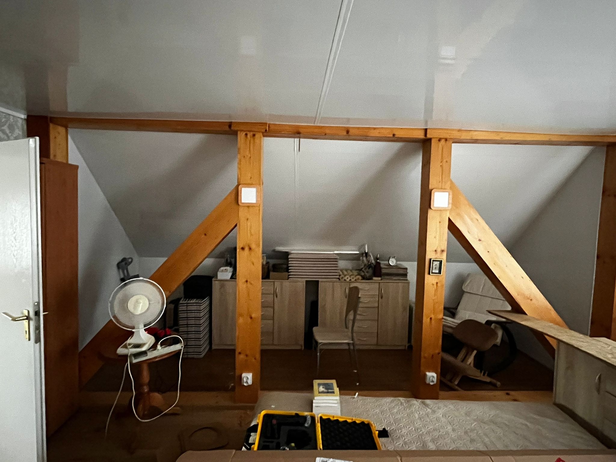 Poddasze w trakcie adaptacji: widoczne drewniane belki konstrukcyjne, meble i sprzęty. Przygotowania do wykończenia wnętrza.