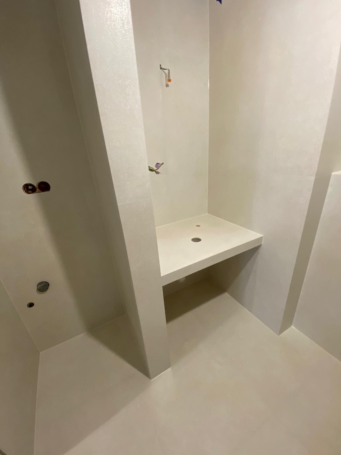 Jasna łazienka z wnęką prysznicową i siedziskiem z otworem odpływowym. Widoczne przygotowane punkty elektryczne i hydrauliczne. Minimalistyczny design.