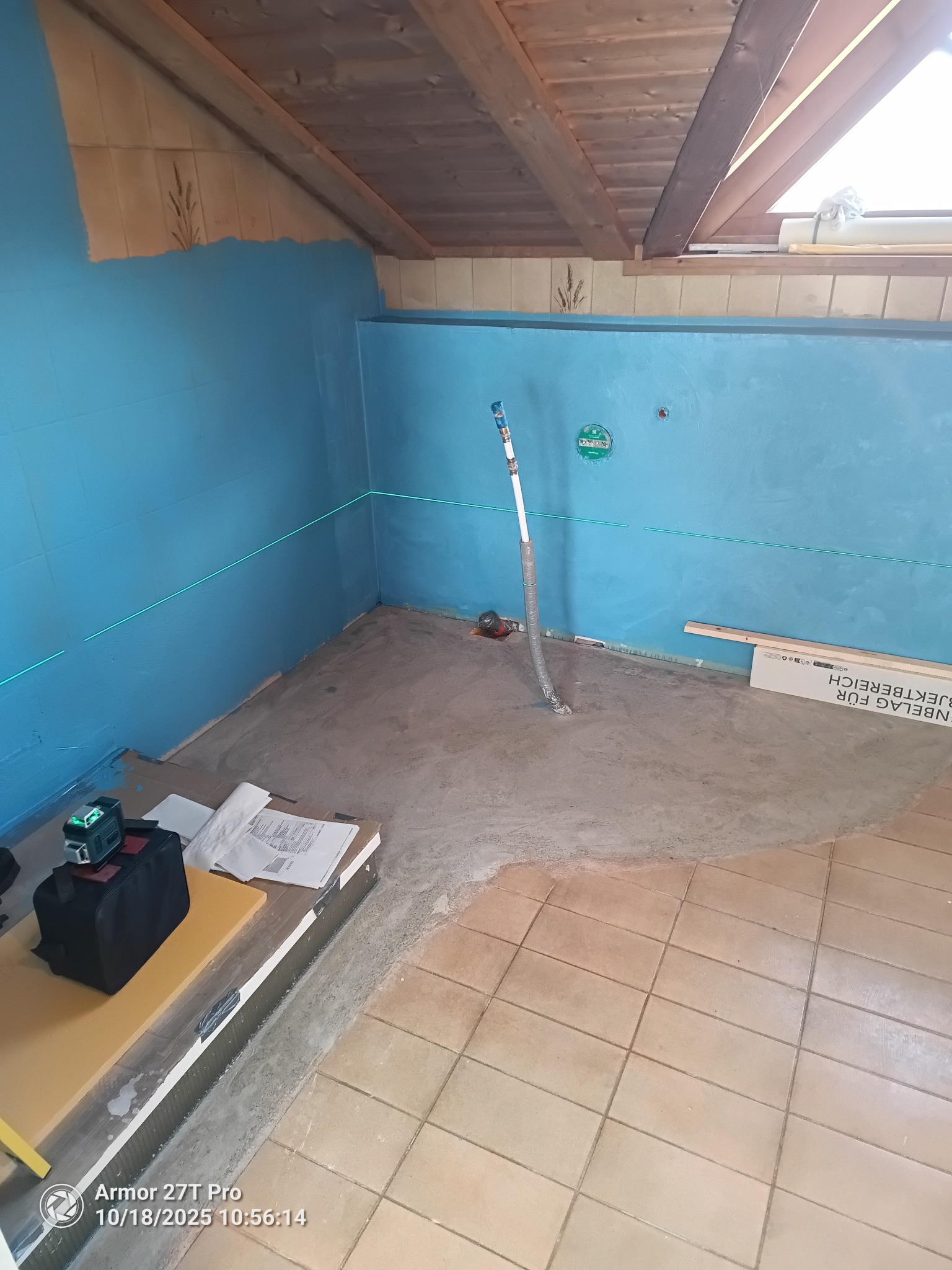 Remont łazienki na poddaszu: niebieskie ściany, wylewka, poziomica laserowa, fragment starej podłogi z płytek. Widoczne narzędzia i materiały budowlane.