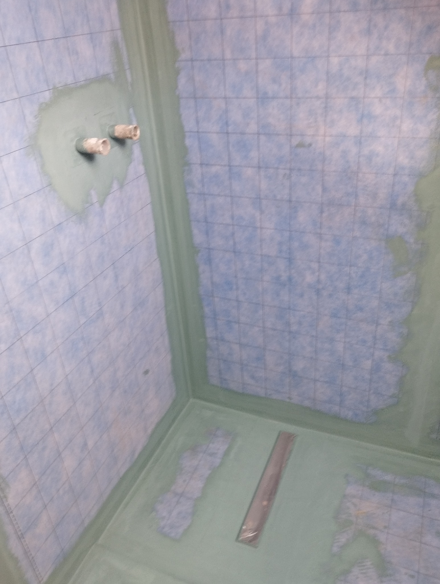 Przygotowana do hydroizolacji kabina prysznicowa z odpływem liniowym i wystającymi rurami. Ściany i podłoga pokryte folią w płynie z siatką wzmacniającą.