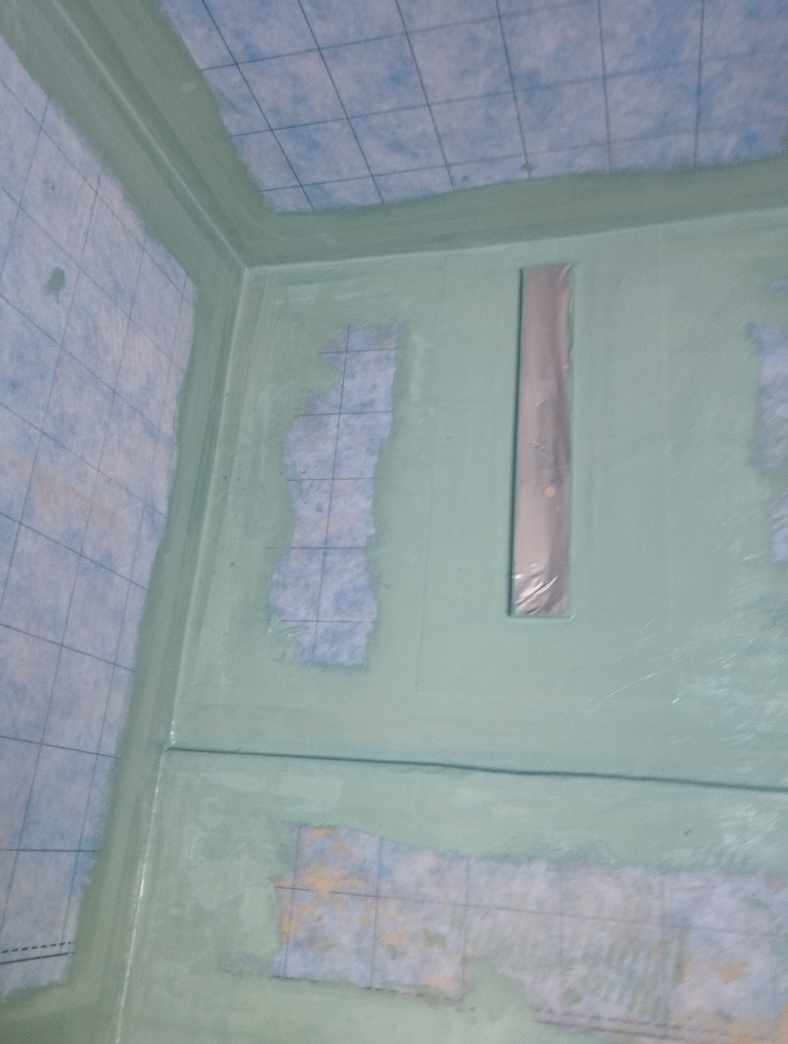 Hydroizolacja w kabinie prysznicowej z widoczną folią w płynie i taśmą uszczelniającą. Etap prac przed położeniem płytek.