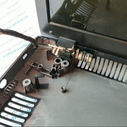 MMSerwis - Wnętrze obudowy laptopa z widocznymi elementami mocowania zawiasu i przewodami. Widoczne ślady naprawy i demontażu. Dokument z instrukcją w tle.