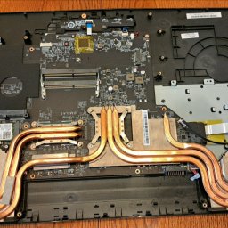 MMSerwis - Otwarty laptop z widoczną płytą główną, systemem chłodzenia z miedzianymi rurkami cieplnymi i wentylatorami. Widoczne elementy elektroniki i narzędzia.