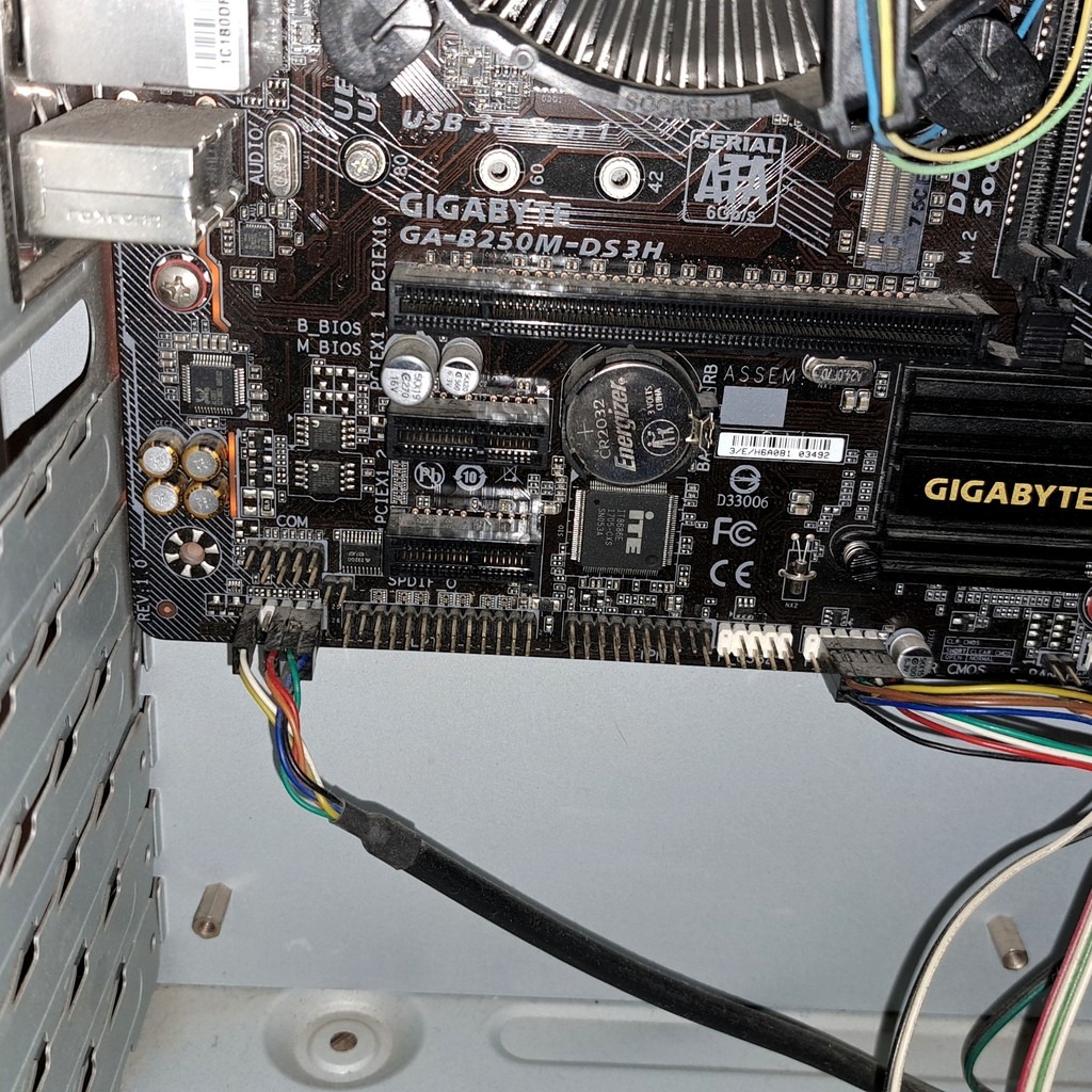 Płyta główna Gigabyte GA-B250M-DS3H w obudowie komputera, widoczne złącza, kondensatory i bateria CR2032. Kabel z kolorowymi przewodami podłączony do płyty.