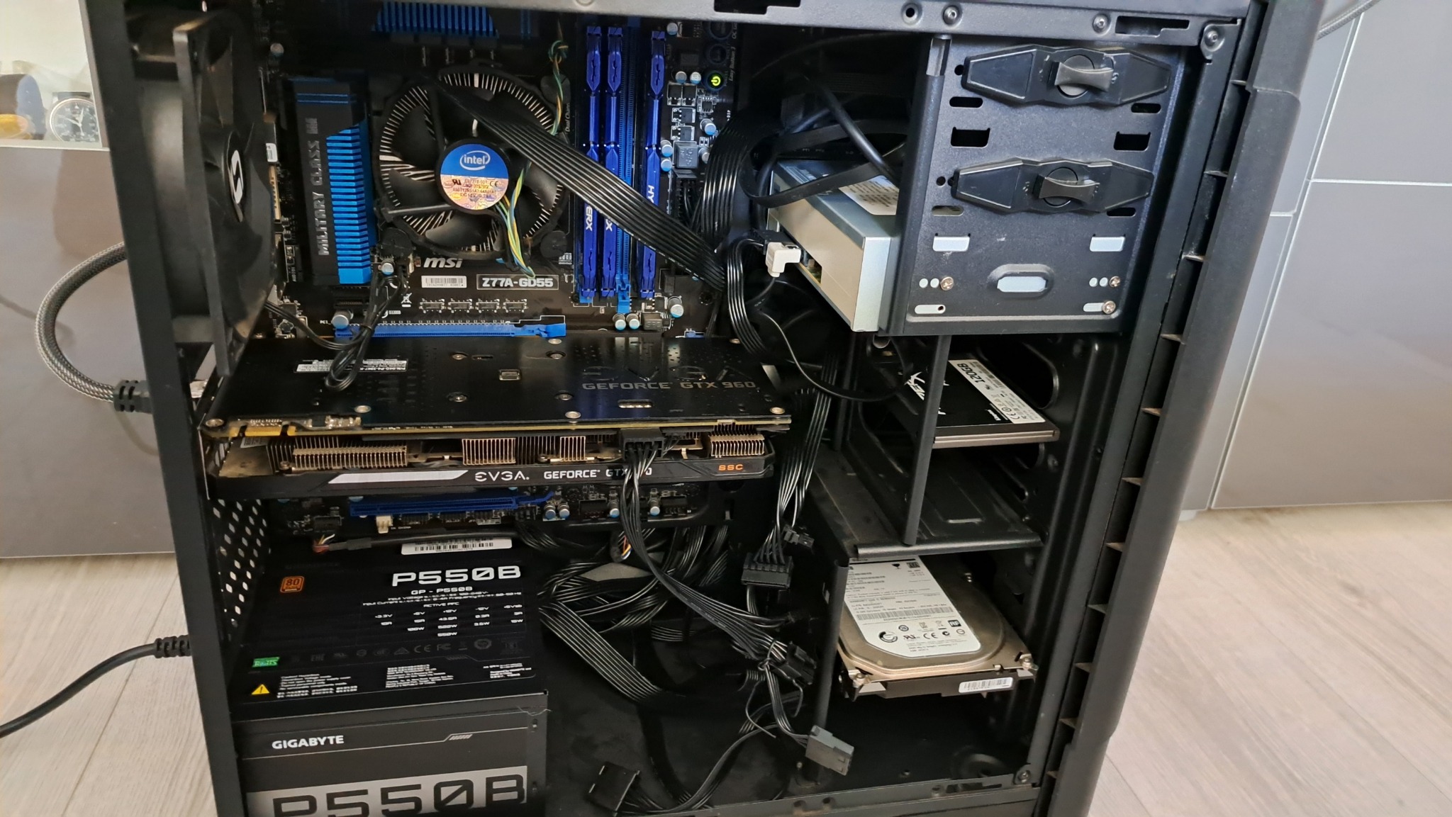 Wnętrze obudowy komputera stacjonarnego z widoczną płytą główną MSI Z77A-GD55, kartą graficzną GeForce GTX 960, zasilaczem Gigabyte P550B i dyskami twardymi.