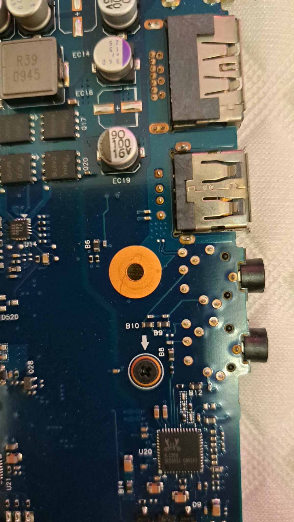 Fragment płyty głównej laptopa z widocznymi elementami elektronicznymi, portami USB i audio. Detaliczne ujęcie z bliska, ukazujące skomplikowaną strukturę układu.