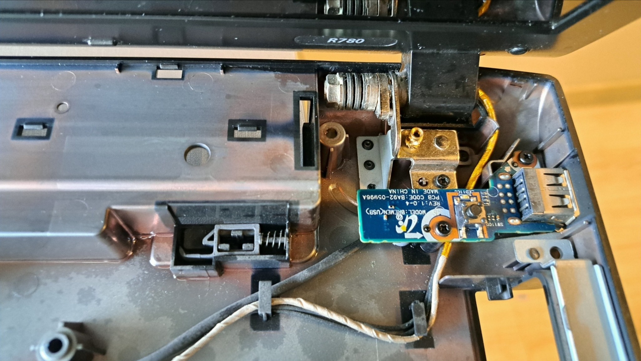 Wnętrze rozłożonego laptopa z widoczną płytką USB, kable i elementy mocujące. Detaliczny widok na port USB w trakcie naprawy lub diagnostyki.