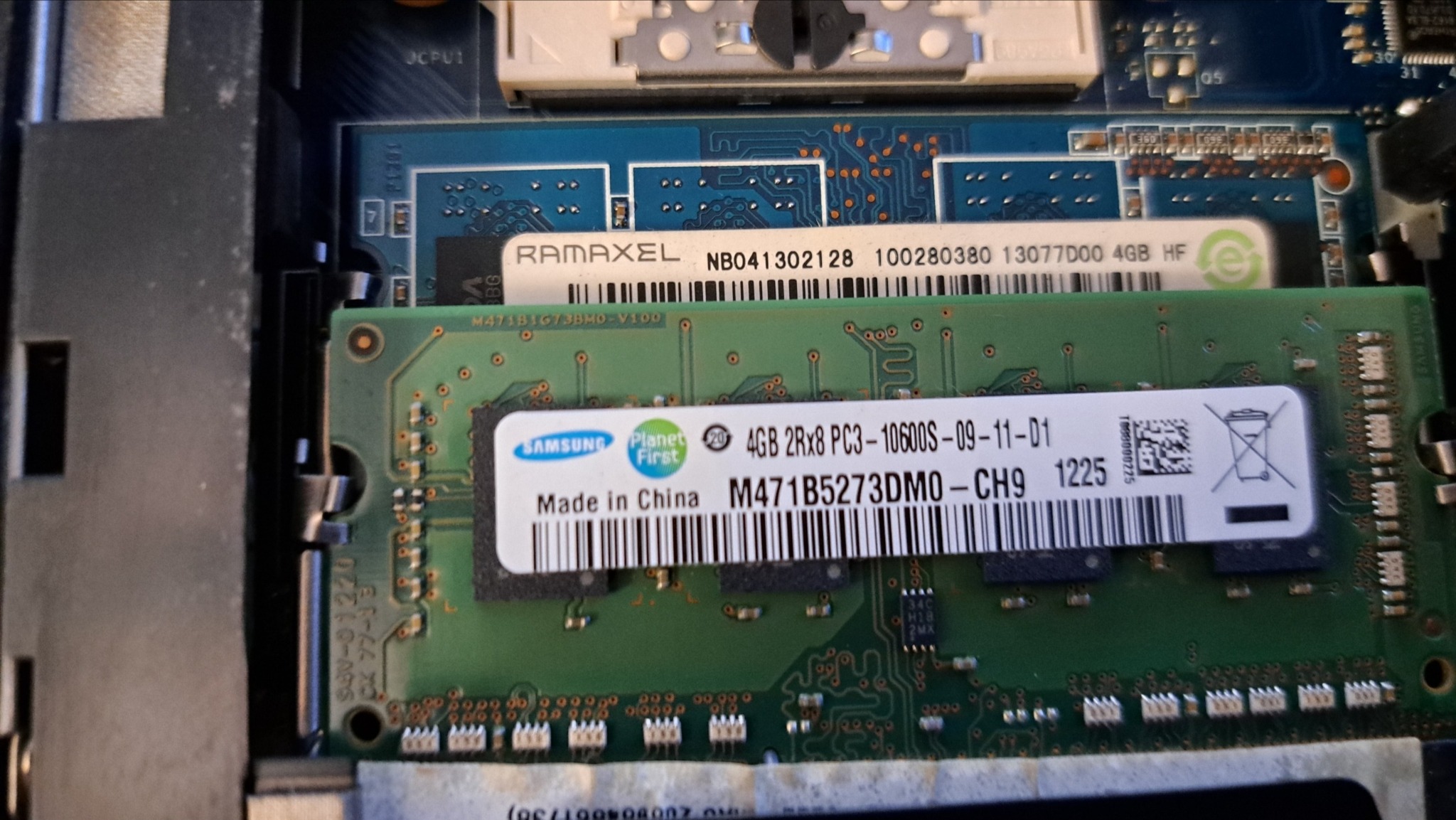 Wnętrze komputera z widocznymi modułami pamięci RAM Samsung i Ramaxel. Zielona płytka drukowana z elementami elektronicznymi. Detal z bliska, ostre światło.