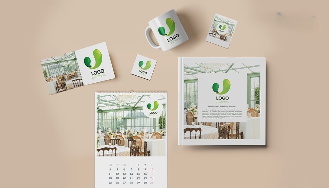 Zestaw materiałów reklamowych z identycznym logo: kalendarz, kubek, wizytówki, podkładka i folder, na beżowym tle. Prezentacja spójnej identyfikacji wizualnej firmy.