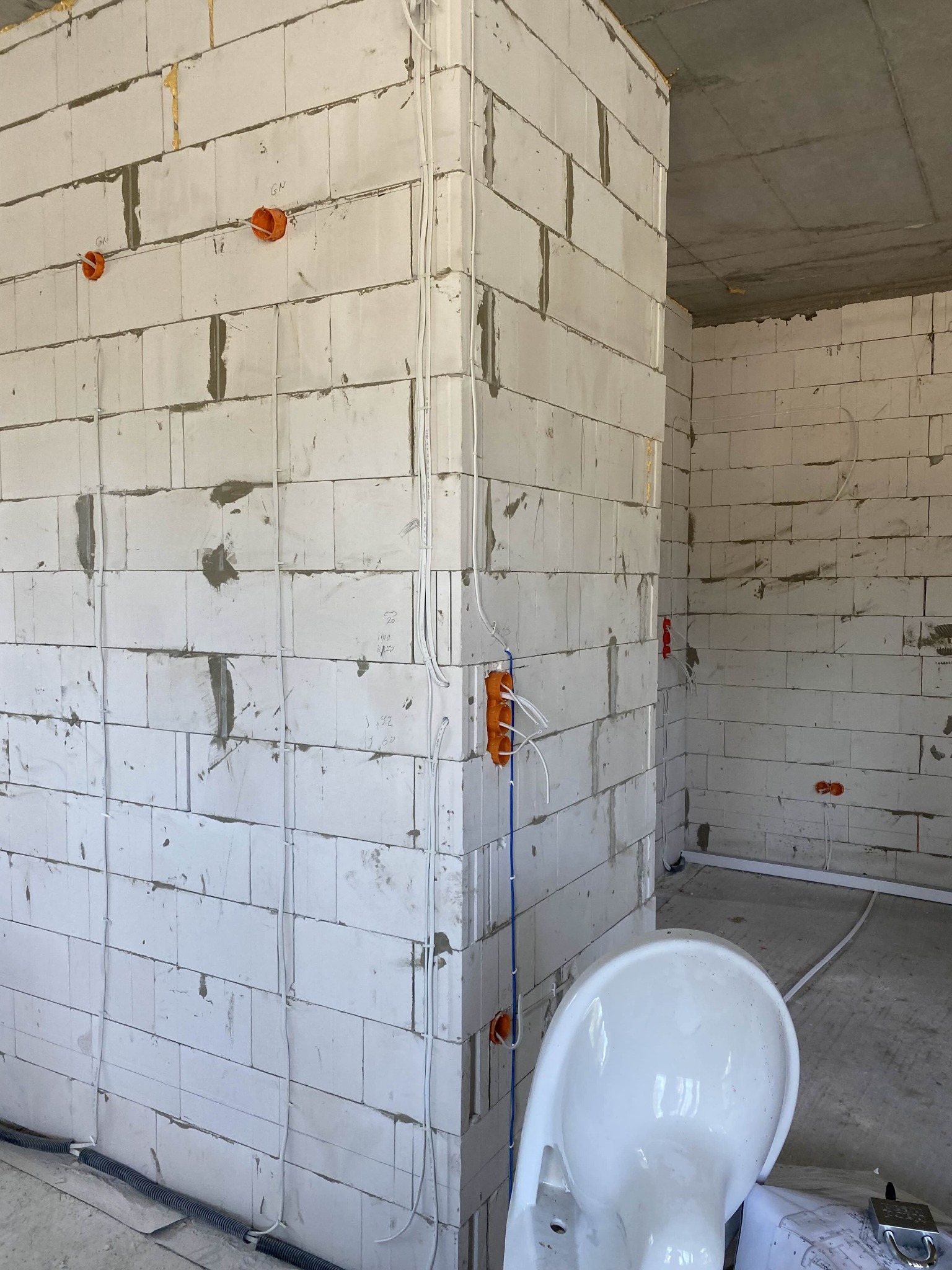 Wewnętrzne ściany z betonu komórkowego z widoczną instalacją elektryczną: kable, puszki. Częściowo widoczna toaleta i plany. Surowy stan wykończenia wnętrza.