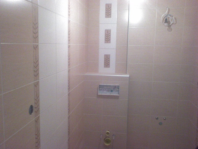 Wykończona łazienka z beżowymi płytkami, dekoracyjnymi wstawkami z motywem roślinnym i zainstalowaną armaturą podtynkową.