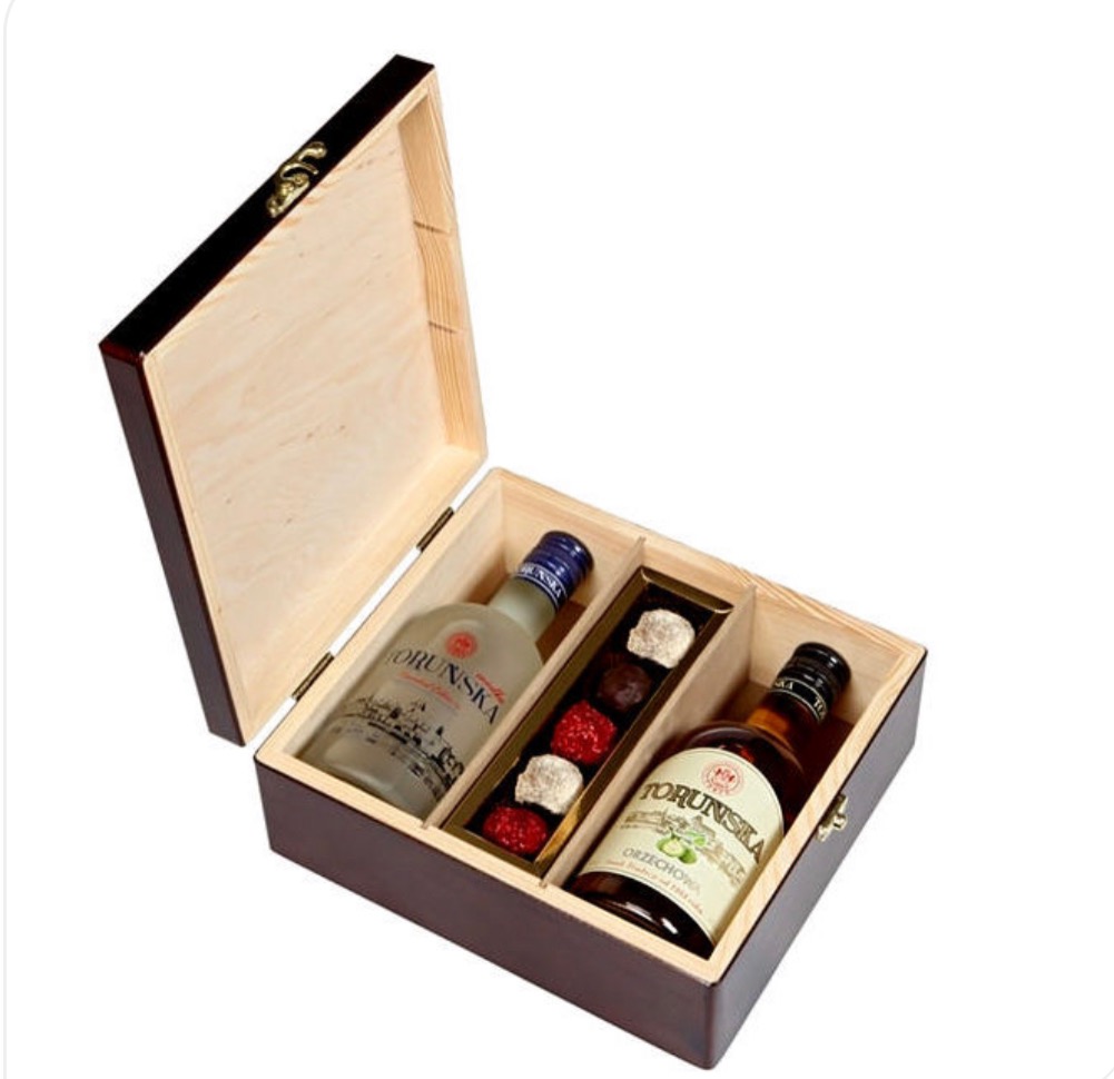 Otwarta, drewniana skrzynka prezentowa z dwoma butelkami Toruńskiej i czekoladkami, widok z góry, oświetlenie studyjne.