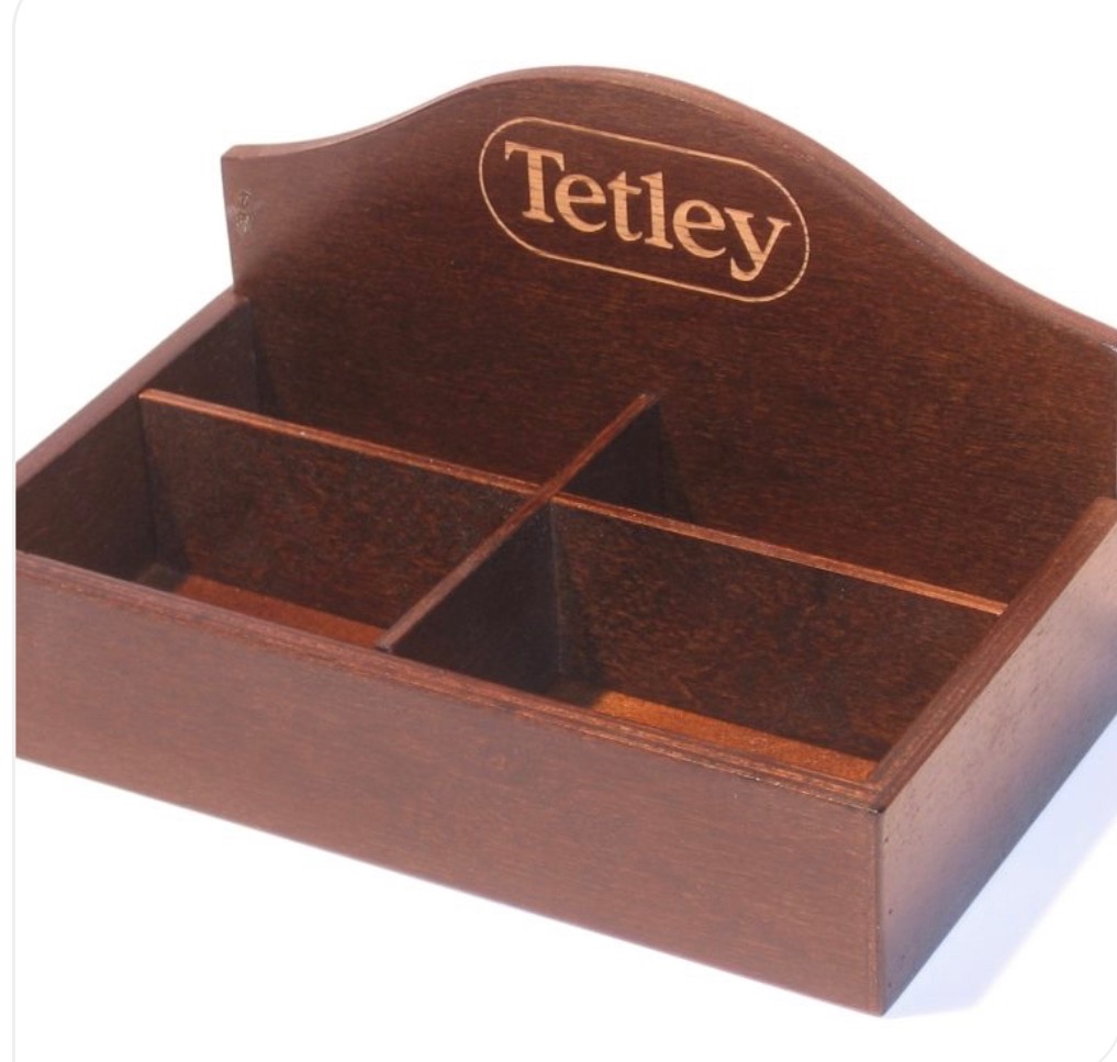 Drewniany organizer na herbatę Tetley z czterema przegródkami, widok z góry pod kątem. Prosty design, ciepłe oświetlenie podkreśla fakturę drewna.