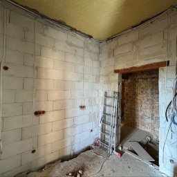 Jarosław Balaka - Pomieszczenie w trakcie remontu z niezakończoną instalacją elektryczną: widoczne przewody w peszlach, puszki na białych bloczkach. W tle drabina i ceglana ściana.