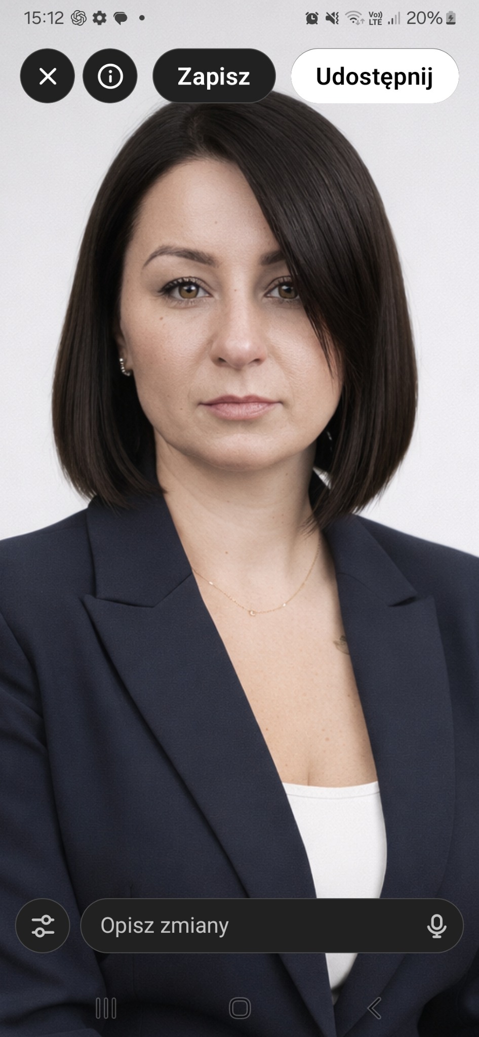 Portret kobiety w granatowej marynarce, z krótkimi, ciemnymi włosami i delikatną złotą biżuterią, na jasnym tle. Profesjonalny wizerunek.