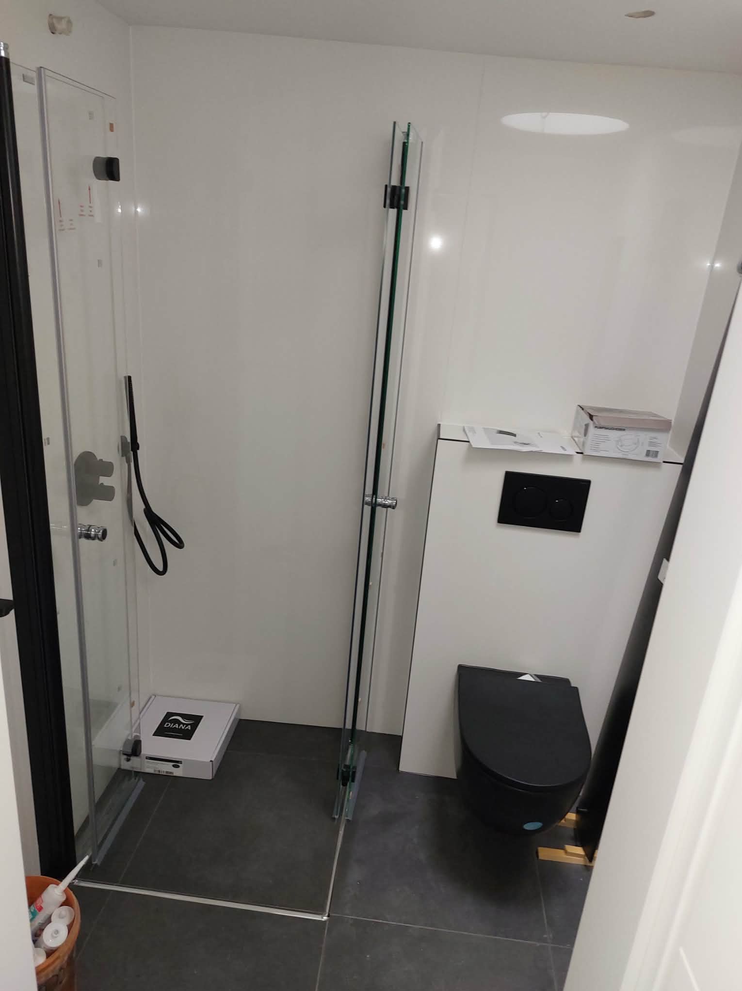 Nowoczesna kabina prysznicowa z czarnymi elementami i podwieszana toaleta w wykończonej łazience w Łęcznej. Minimalistyczny design, szklane ścianki kabiny.