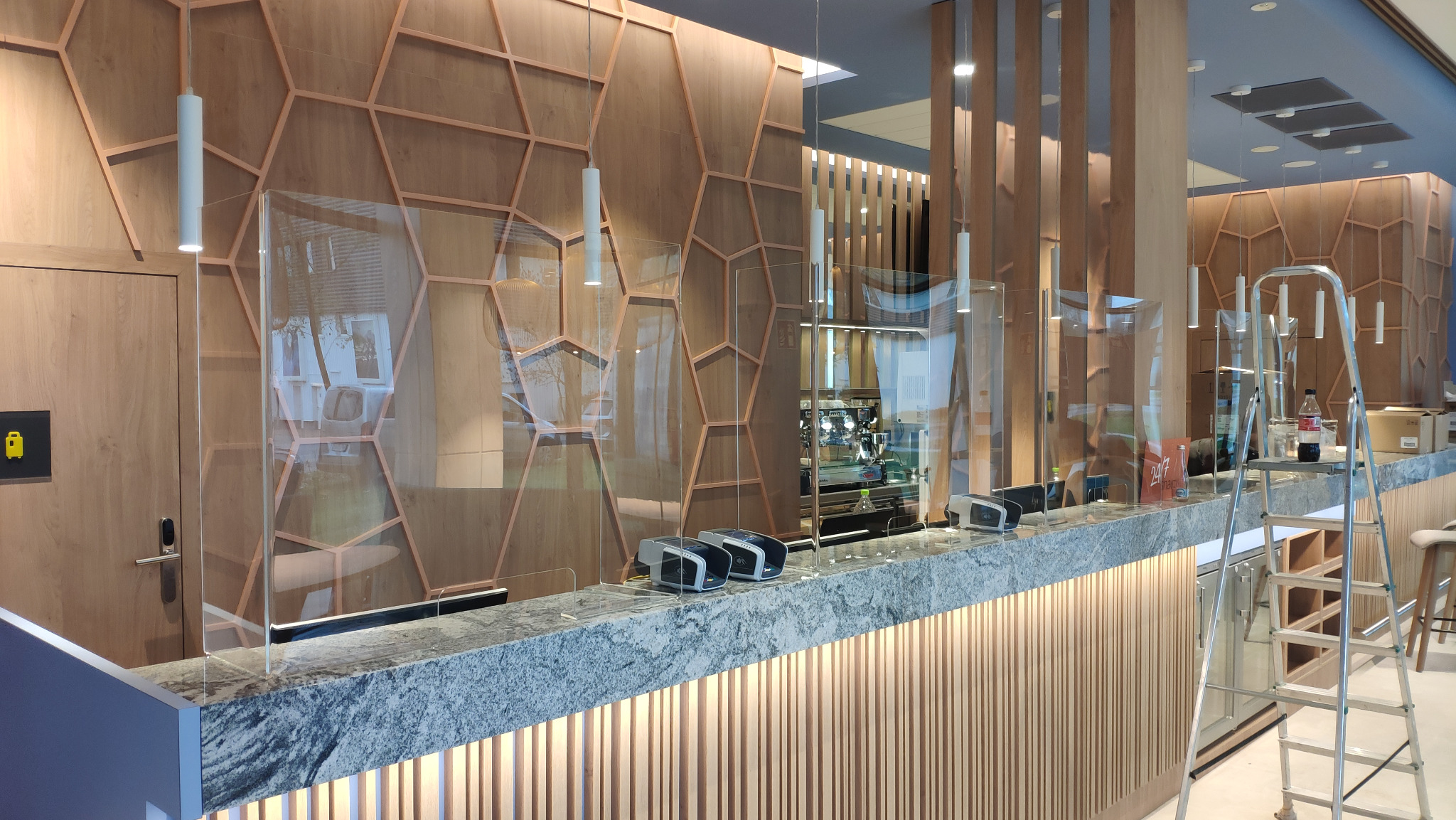 Nowoczesna recepcja z drewnianą ścianą w heksagony i szklanymi przegrodami ochronnymi, widok z boku, Warszawa. Marmurowy blat i designerskie oświetlenie.