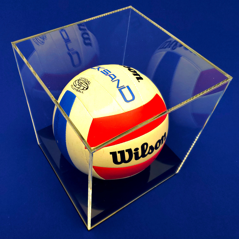 Piłka do siatkówki Wilson w przezroczystej, akrylowej gablocie na ciemnoniebieskim tle. Precyzyjne wykonanie, ostre krawędzie, widoczne odbicia światła.