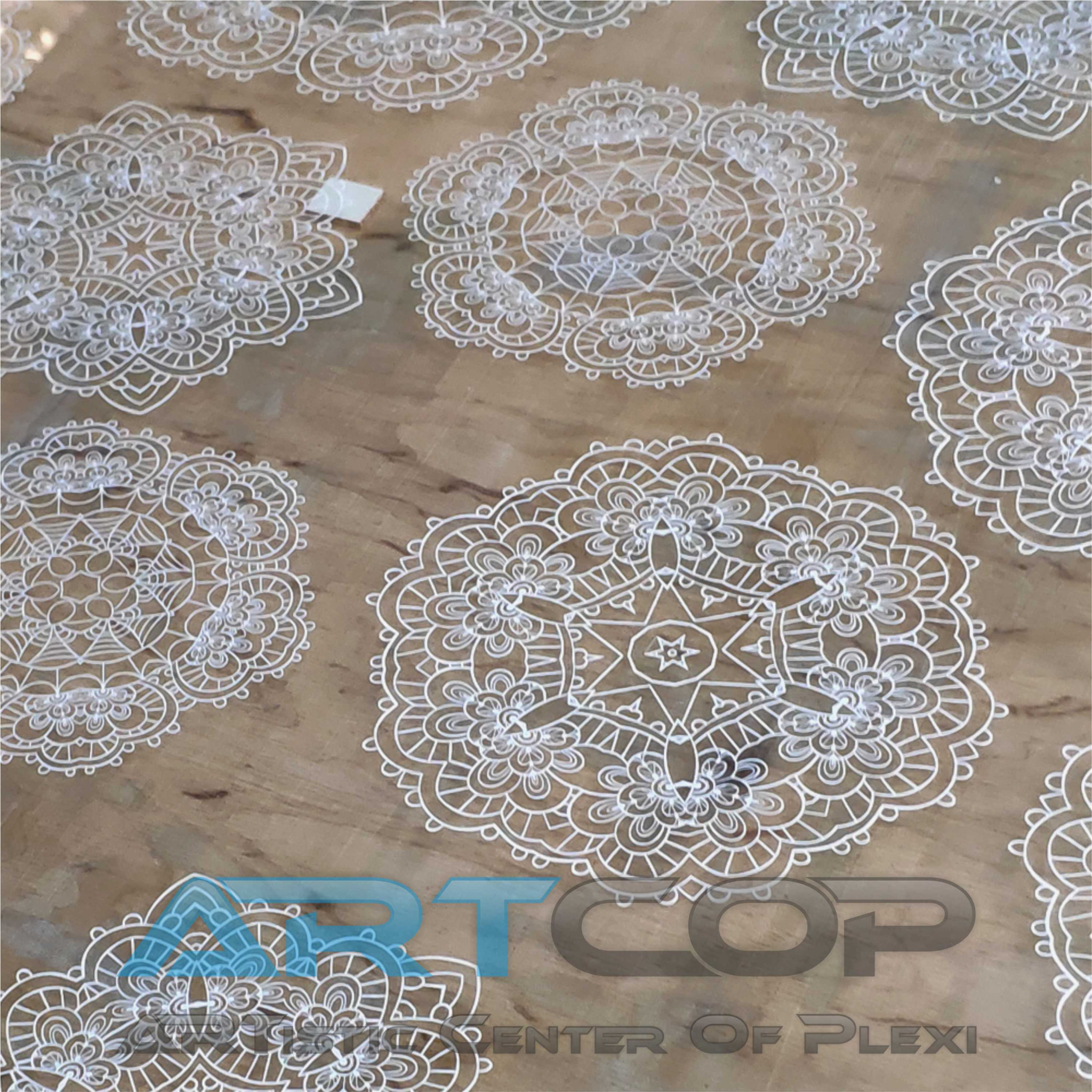 Białe, ażurowe mandale wycięte laserowo na brązowym tle, z widocznym logo firmy ARTCOP CENTER OF PLEXI. Precyzyjna obróbka CNC.