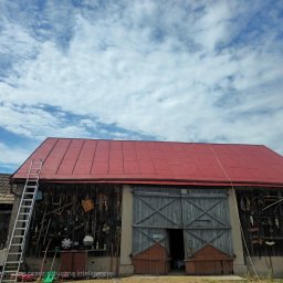 Czas na Mycie - Czerwony dach stodoły pod błękitnym niebem z chmurami. Metalowa drabina oparta o ścianę. Na ścianie narzędzia i sprzęty. Otwarta brama z szarego drewna.