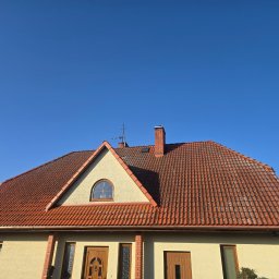 Czas na Mycie - Dom jednorodzinny z czerwoną dachówką i beżową elewacją, widoczny z dołu na tle błękitnego nieba. Charakterystyczne okrągłe okno na poddaszu.