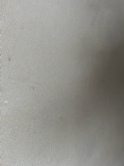 Gładka, jasnoszara powierzchnia ściany po nałożeniu gładzi, z delikatną fakturą i subtelnym cieniowaniem światła. Minimalistyczne ujęcie detalu wykończenia wnętrza.