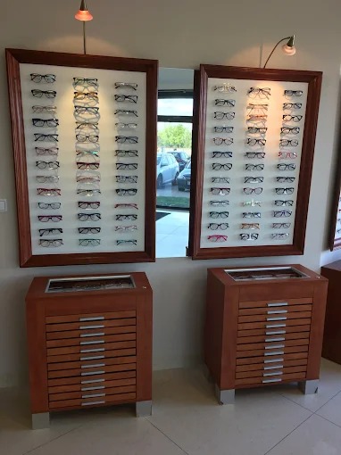 Salon optyczny: ekspozycja okularów korekcyjnych w drewnianych ramkach, uzupełniona szafkami z szufladami. Widoczne odbicie w lustrze.