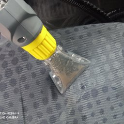 NataGroup - Czyszczenie tapicerki samochodowej przy użyciu odkurzacza piorącego z przezroczystą końcówką, ukazującą brudną wodę. Widoczna struktura materiału.