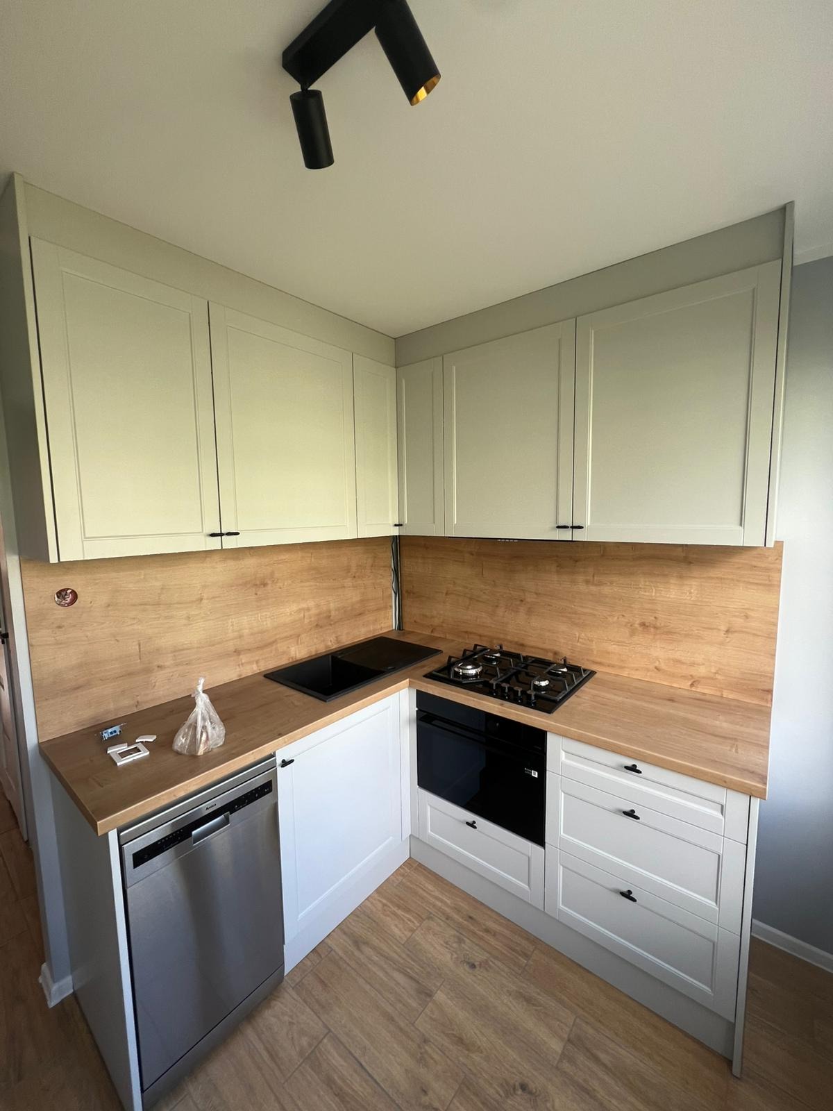 Jasna kuchnia w stylu skandynawskim z drewnianym blatem i sprzętami AGD: płyta gazowa, piekarnik, zmywarka. Minimalistyczne oświetlenie punktowe.