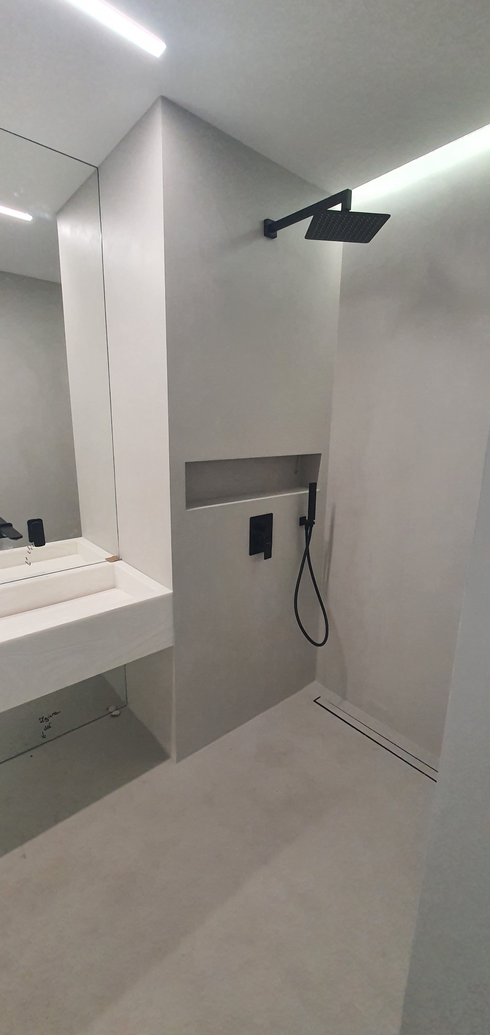 Minimalistyczna łazienka w odcieniach szarości z czarną armaturą: deszczownica, bateria podtynkowa i odpływ liniowy. Umywalka nablatowa z lustrem.