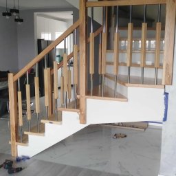 Almar - Jasne drewniane schody z metalowymi balustradami w nowoczesnym wnętrzu. Widoczne narzędzia sugerują trwający montaż. Marmurowe płytki podłogowe.