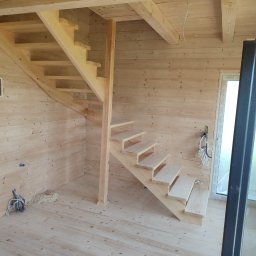 Almar - Jasne, drewniane schody spiralne w surowym wnętrzu z boazerią. Widoczne narzędzia i kable, co sugeruje etap montażu. Naturalne światło podkreśla fakturę drewna.