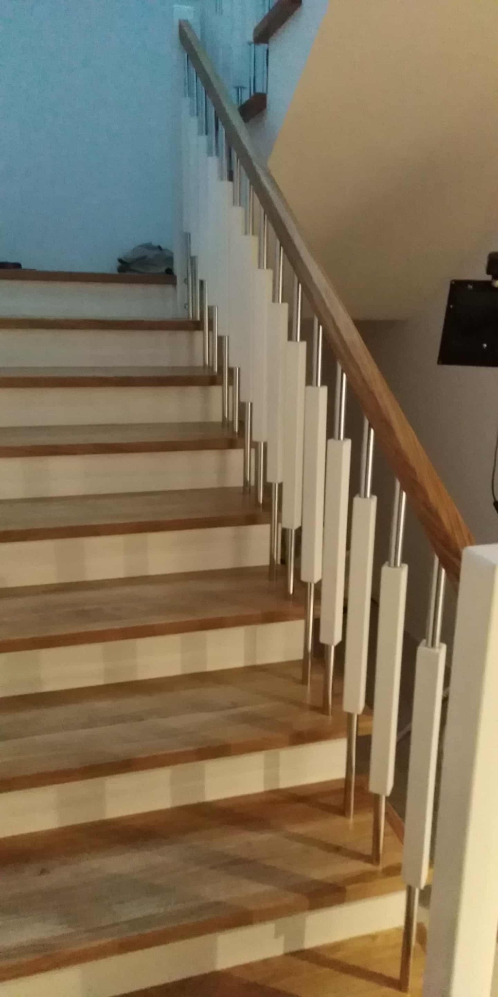 Drewniane schody z białymi balustradami i metalowymi elementami, widok z dołu. Naturalne oświetlenie podkreśla strukturę drewna i nowoczesny design.