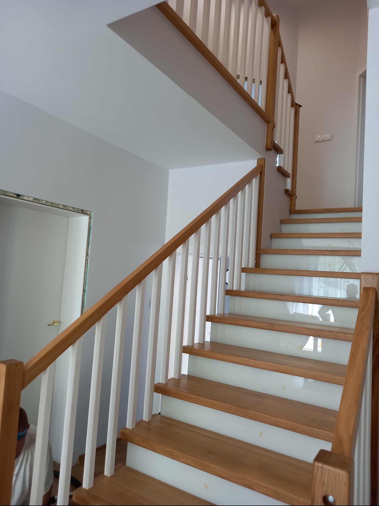 Drewniane schody z białymi balustradami i podstopnicami z mlecznego szkła, widok z dołu. Naturalne oświetlenie, minimalistyczny design. Detal wykończenia wnętrza.