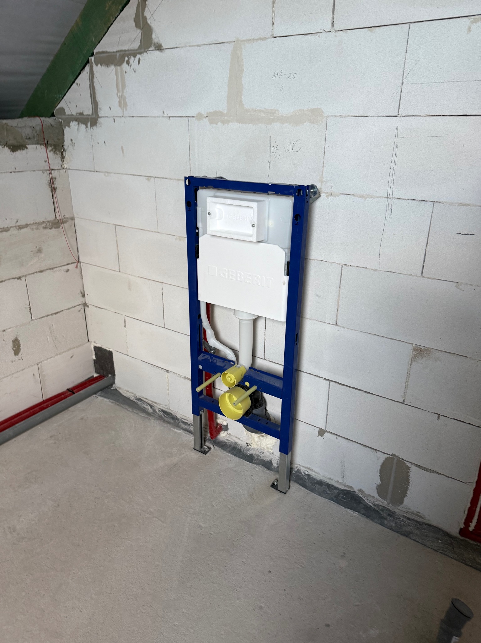 Stelaż podtynkowy Geberit Duofix zamontowany przy ścianie z betonu komórkowego, widoczne rury instalacyjne. W tle poddasze ze skosem.