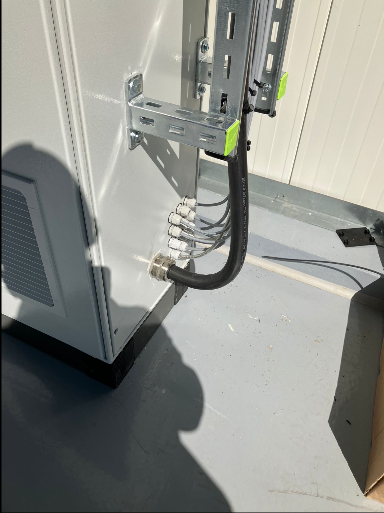 Szara szafa sterownicza z zamontowanymi przewodami i uchwytami, widoczne złącza i kable. Instalacja wykonana schludnie, w jasnym pomieszczeniu.