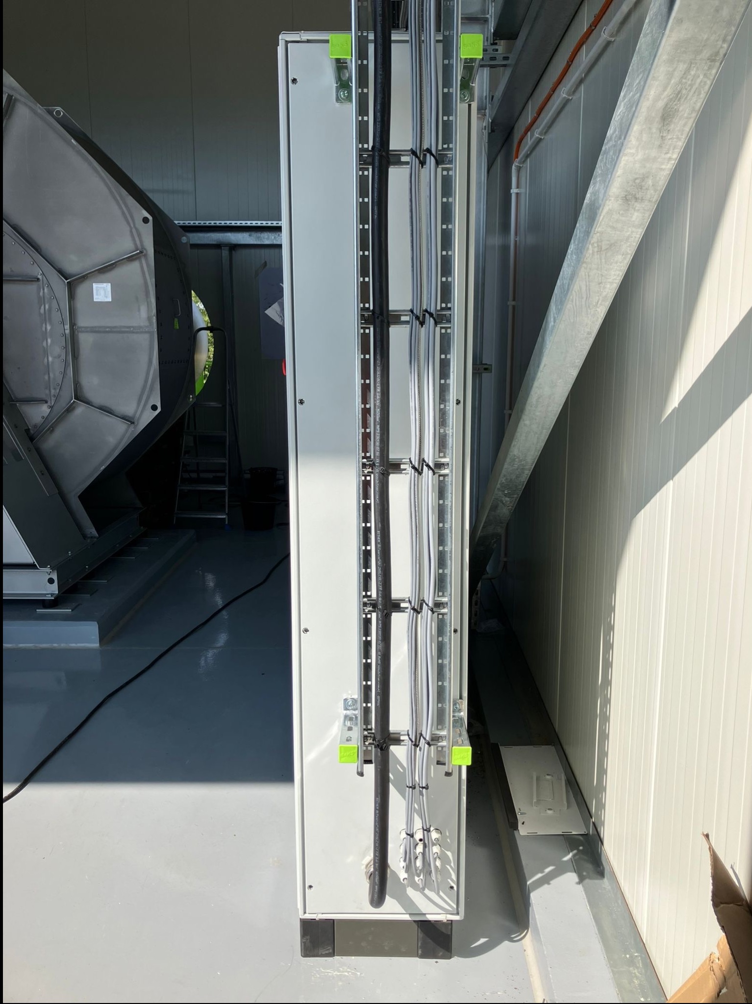 Wnętrze hali z zamontowaną szafą sterowniczą i poprowadzonymi kablami w korytkach. Widoczny fragment wentylatora i konstrukcja wsporcza.