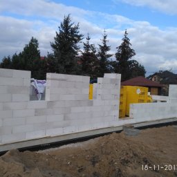 P.W. MIREX - Wznoszenie ścian domu z białych bloczków Ytong, widoczne żółte opakowania bloczków, w tle drzewa i zabudowania.