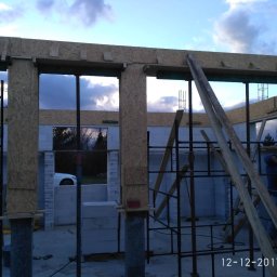 P.W. MIREX - Budowa domu w trakcie: murowane ściany z betonu komórkowego, drewniane szalunki okienne, stalowe rusztowania, widoczny pracownik w kurtce.