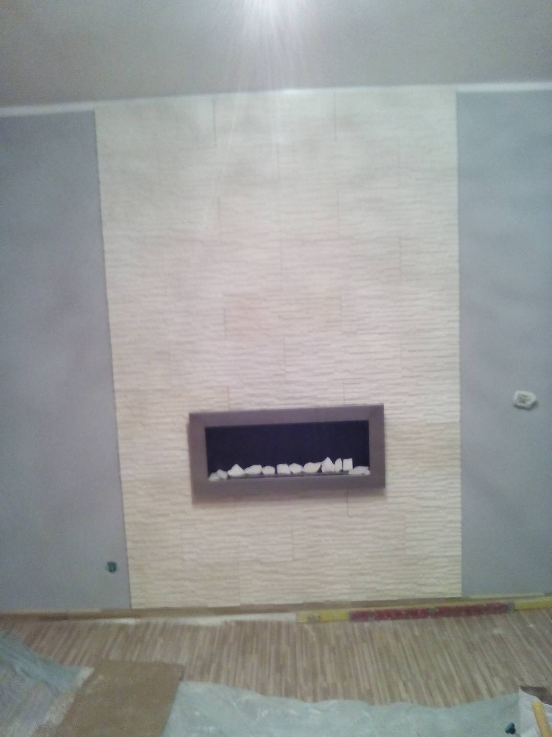 Ściana z dekoracyjnym panelem imitującym kominek i wykończeniem w Świebodzicach, widoczne fragmenty podłogi w trakcie prac.