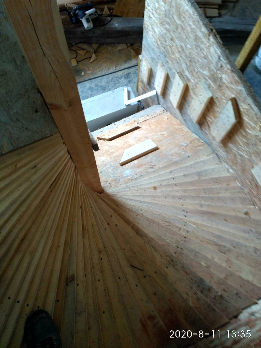 Konstrukcja schodów spiralnych w trakcie montażu, widoczne drewniane elementy i narzędzia w tle.