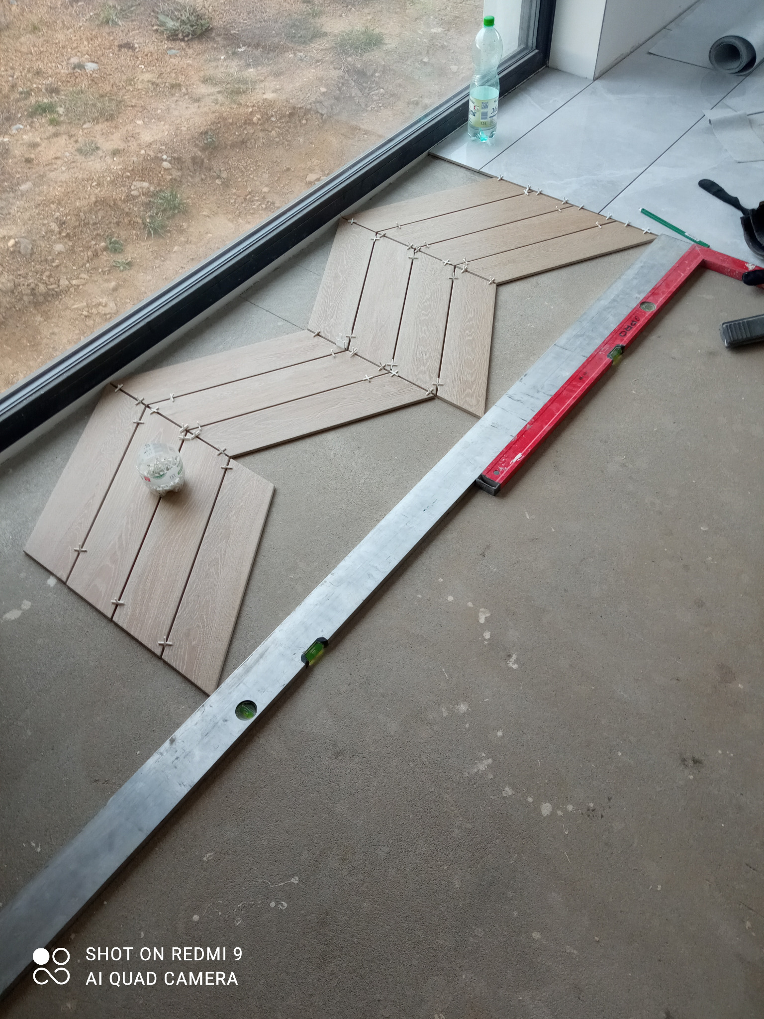 Układanie paneli podłogowych w jodełkę, widoczne płytki z dystansami, poziomica i częściowo ułożona podłoga przy oknie.